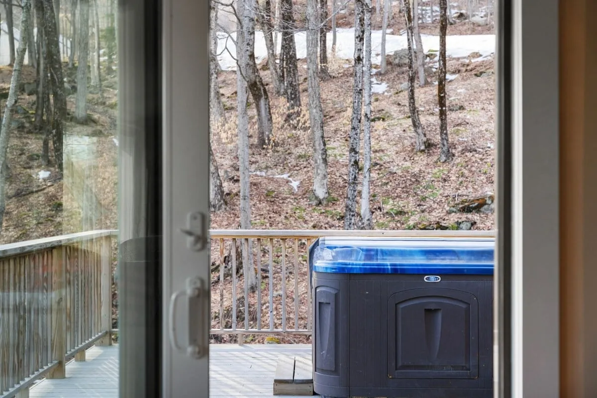 This image showcases the hot tub on a wooden deck, enveloped by forest views through glass railings. The setting highlights the peaceful immersion in nature, with the hot tub as the focal point, perfect for stargazing or unwinding after outdoor adventures.