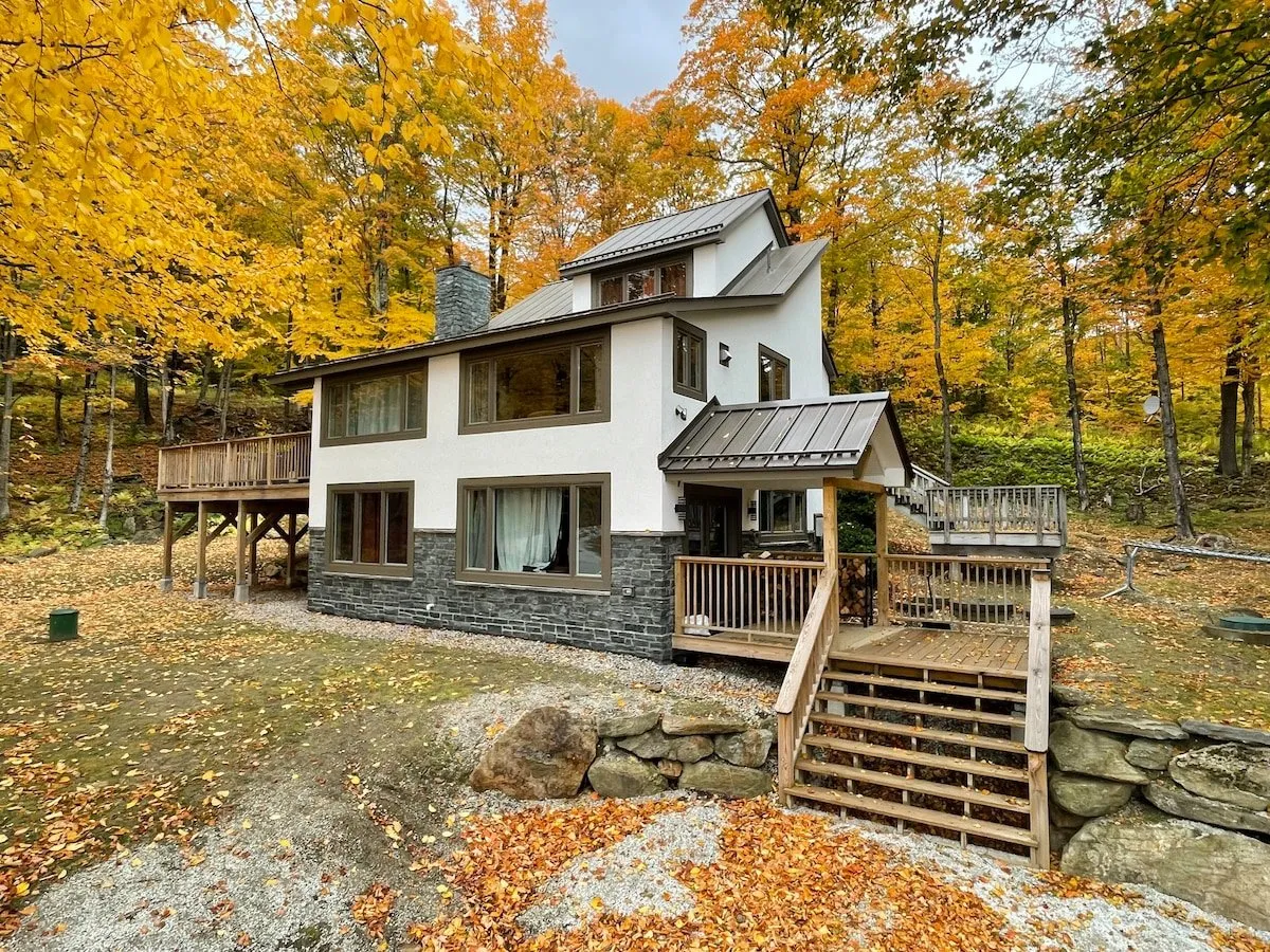 This exterior shot captures the modern architecture of the house set against vibrant autumn foliage, with an inviting outdoor deck area. The scene suggests easy outdoor access and a strong connection to the natural landscape that surrounds the property.