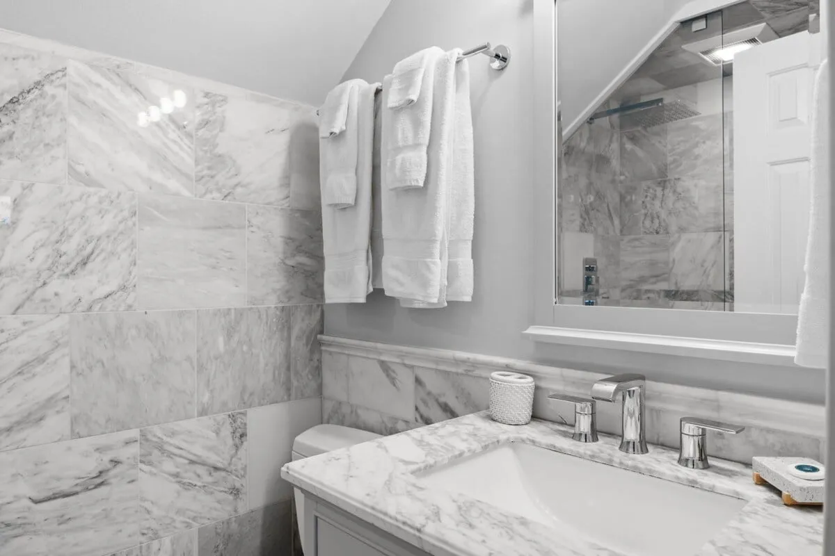 A modern bathroom featuring a sleek marble sink, round mirror, plush towels, and contemporary fixtures. The clean, minimalist design creates a sense of freshness and tranquility.